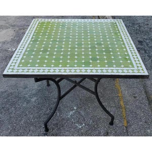 May include: Square outdoor table with a green and white tiled top. The table has a dark metal frame and legs. The tabletop is approximately 91 cm square.
