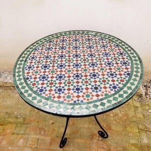 May include: A round mosaic tile table with a black wrought iron base. The tabletop features a colorful geometric pattern in red, blue, green, and white. The table is approximately 36 inches in diameter.