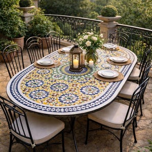 May include: An outdoor dining set with an oval mosaic tile table. The table has a colourful floral pattern and is surrounded by black metal chairs with cream cushions. A lantern and flowers decorate the table, set on a stone patio.