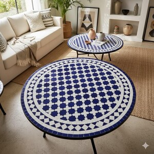 May include: Two round coffee tables with blue and white mosaic tile tops and black metal legs. The tables are in a living room setting with a white sofa, a woven rug, and decorative items.