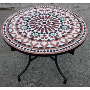 May include: Round mosaic tile table with a black metal base. The tabletop features a geometric pattern in red, white, black, and teal. The table is approximately 40 inches in diameter.