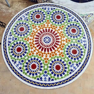 May include: A circular mosaic table top with a colourful geometric design. The pattern includes a central starburst in red and orange, encircled by blue, green, and yellow floral shapes. The table top is approximately 91 cm in diameter.