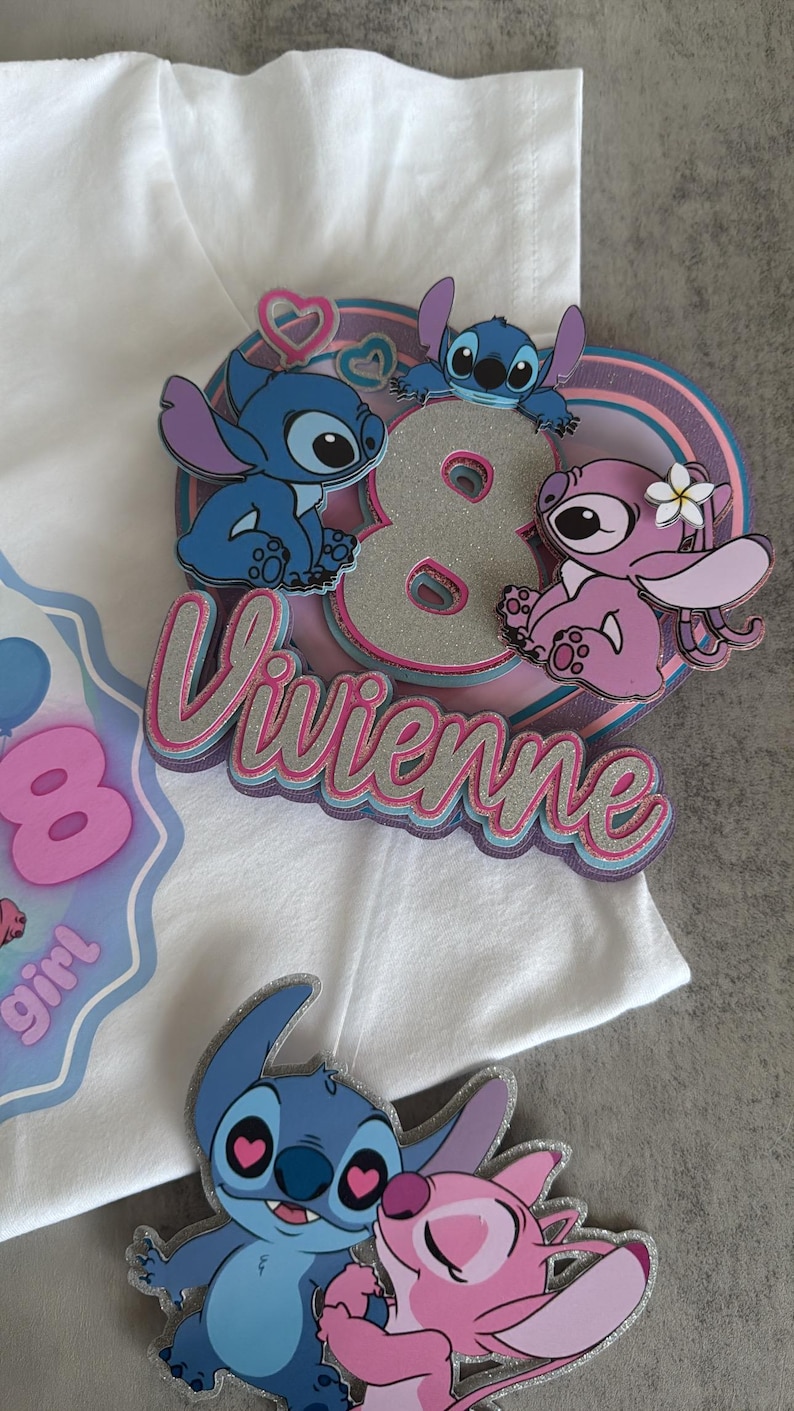 May include: A white t-shirt with a pink, blue and silver glitter appliqu&eacute; featuring the number 8, the name "Vivienne", and three Stitch characters. The Stitch characters are blue, pink and blue with pink hearts for eyes.