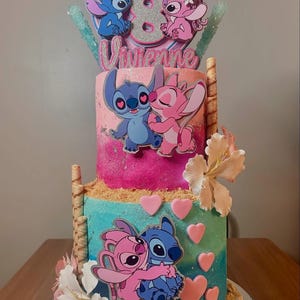 May include: A two-tiered cake decorated with a blue and pink Stitch and Angel theme. The cake is decorated with hearts, flowers, and a topper that says "Vivienne" and features Stitch and Angel.