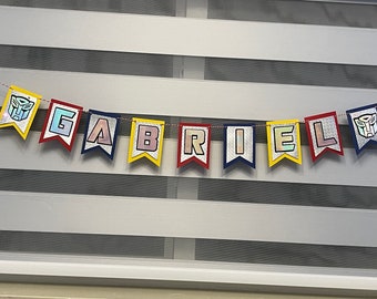 May include: A colorful banner with the name "GABRIEL" spelled out in individual flags. Each flag has a different color and features a robot-like design.