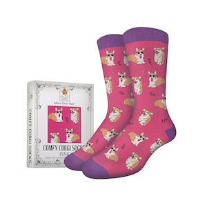 Puede incluir: Calcetines rosas con un estampado de perros corgi con gafas de sol y un diseño en zigzag. Los calcetines tienen puños y punteras moradas. Una caja de calcetines está a la izquierda con el texto "COMFY CORGI SOCKS PINK".