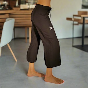 May include: Black cropped pants with a drawstring waist and a small square patch on the pocket. The pants have a wide leg and are made of a lightweight fabric. The pants are shown in a lifestyle setting.