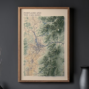 May include: A framed topographic map of Portland and the Cascades, featuring a detailed relief of the landscape. The map is in a wooden frame and displays the city's layout with blue river lines and roads. The text "PORTLAND AND THE CASCADES" is at the top.