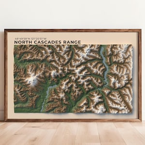 May include: A framed topographic map of the North Cascades Range, featuring detailed relief shading in shades of brown, green, and white. The map includes the text "NORTH CASCADES RANGE" and coordinates. The frame is made of wood.