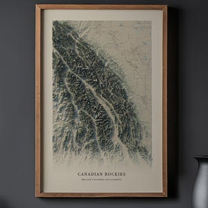 以下が含まれることがあります： カナディアンロッキーのフレーム入りプリント。グレーと白の濃淡で描かれた地形図です。プリントは薄茶色の木製フレームに入っています。「CANADIAN ROCKIES」と「BRITISH COLUMBIA AND ALBERTA」の文字が画像の下部に印刷されています。