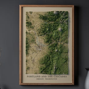 May include: A framed 3D relief map of Portland and the Cascades, Oregon and Washington. The map shows a detailed topographical representation in green and tan, within a wooden frame. The text "Portland and the Cascades" is visible.