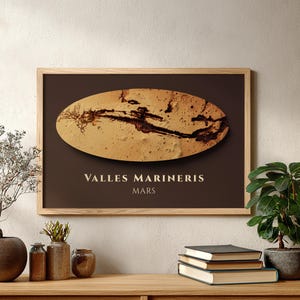 May include: A rectangular framed wall art print featuring a dark brown background with a central horizontal oval displaying a textured tan and dark brown topographical map of Valles Marineris on Mars, with the text Valles Marineris Mars below.