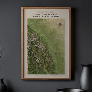 Pode incluir: Uma impressão de arte de parede emoldurada apresentando um mapa topográfico das Montanhas Rochosas canadenses e das planícies de Alberta. O mapa exibe terreno verde e cadeias de montanhas com o texto "BRITISH COLUMBIA & ALBERTA CANADIAN ROCKIES AND ALBERTA PLAINS".
