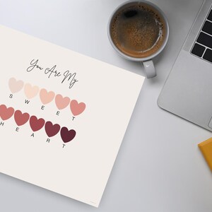 Puede incluir: Una impresi&oacute;n con el texto "You Are My Sweet Heart" sobre una serie de formas de coraz&oacute;n en varios tonos de rosa y rojo. Tambi&eacute;n se ven una taza de caf&eacute;, un port&aacute;til y un bloc de notas.