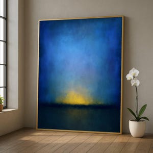 Puede incluir: Gran obra de arte abstracta enmarcada. La obra presenta un degradado de azules, oscureciéndose hacia la parte inferior y aclarando hacia arriba. Una banda horizontal amarilla y dorada sugiere una puesta o salida de sol. El marco es dorado.