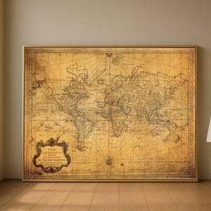 Puede incluir: Un mapa del mundo antiguo enmarcado con un marco dorado. El mapa está en tonos sepia, con cartografía detallada y texto en francés. El mapa se muestra en una pared marrón claro y un suelo de madera.