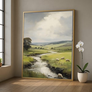 May include: A framed landscape painting depicts a serene pastoral scene. A stream meanders through a green field where several sheep graze. The sky is overcast, and the painting is framed in gold.