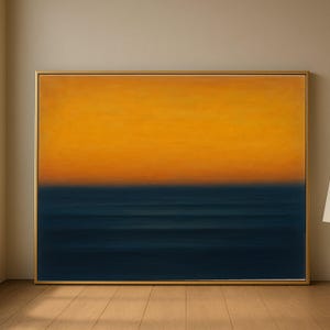 Puede incluir: Pintura abstracta con marco dorado. La obra presenta un degradado de colores, con un amarillo-naranja brillante en la parte superior que se transforma en un azul marino profundo en la parte inferior, creando un efecto de horizonte. La pintura se exhibe sobre un suelo de madera.
