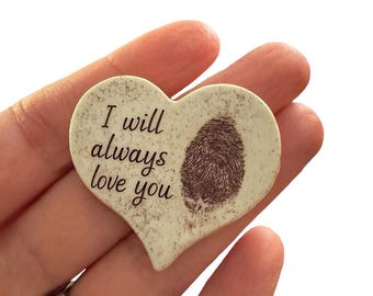 May include: Heart-shaped keepsake with a fingerprint and the words "I will always love you" in black script. The keepsake is off-white with a textured surface.