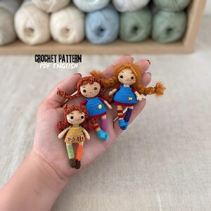 May include: Three small crocheted dolls with reddish-brown yarn hair, wearing colorful dresses and mismatched socks. The dolls feature embroidered facial details and are presented as a crochet pattern PDF English.