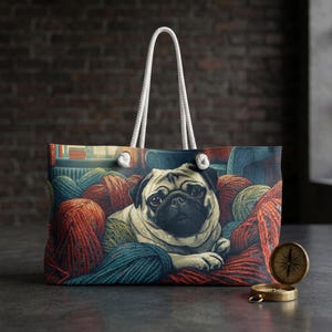 May include: Tote bag with a pug illustration nestled amongst balls of yarn in shades of red, blue, and green. The bag has a white rope handle. A brass compass is on the surface. The bag's design is reminiscent of a cozy craft room.