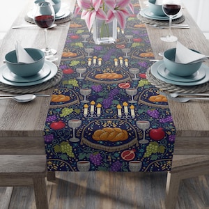 May include: A navy blue table runner with a repeating pattern of challah bread, grapes, pomegranates, candles, and goblets. The runner is set on a wooden table with place settings, wine glasses, and a vase of pink flowers.