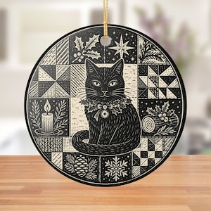 May include: A round black and white ceramic ornament featuring a central illustration of a cat wearing a holly collar, surrounded by a grid of holiday motifs including a lit candle, a pinecone, a snowflake, a star, and geometric quilt patterns.