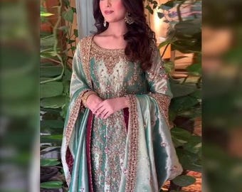 Könnte beinhalten: Ein mintgrünes formelles Kleid mit goldener Stickerei und passendem Schal. Das Kleid hat aufwendige Details am Ausschnitt und an den Ärmeln. Der Schal hat ein bordeauxfarbenes Futter. Das Design ist elegant und für besondere Anlässe geeignet.