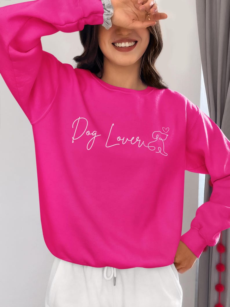 May include: A bright pink sweatshirt with the words "Dog Lover" in cursive script and a dog silhouette with a heart. The sweatshirt is a solid color and has long sleeves.