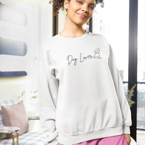 May include: White sweatshirt with the text "Dog Lover" in a script font, along with a small dog silhouette. The person is wearing pink shorts. The background includes a patterned chair and a red rug.