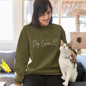 May include: Olive green sweatshirt with the text "Dog Lover" in a cursive font, accompanied by a line drawing of a dog and a heart. The sweatshirt is long-sleeved and made of a soft material.