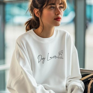 May include: White sweatshirt with the text "Dog Lover" in a script font, accompanied by a small dog illustration. The sweatshirt is a casual style, suitable for everyday wear.