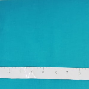 May include: A solid teal fabric with a ruler placed across the bottom. The ruler is white with black markings and numbers. The fabric is a vibrant, solid color, and the ruler measures in inches.