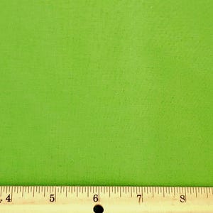 May include: Bright green fabric with a textured surface. A wooden ruler with black markings and white numbers is at the bottom of the image. The ruler is marked in inches.