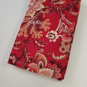 May include: Folded red fabric with a floral pattern in shades of cream, peach, and burgundy. The fabric features a detailed, ornate design with large flowers and swirling leaves. The overall aesthetic is vintage and decorative.