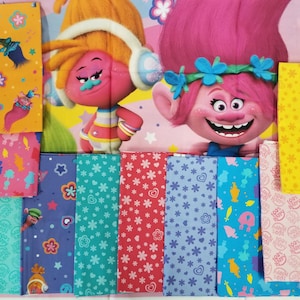 May include: An assortment of colorful fabric pieces featuring characters from the Trolls movie. The fabrics display various patterns with stars, flowers, and character illustrations in shades of pink, yellow, blue, and green.