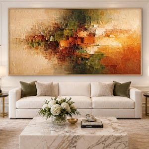 May include: A large rectangular abstract oil painting featuring a textured impasto technique with a color palette of warm orange, deep brown, olive green, and cream tones, displayed in a thin wooden frame above a white sofa in a living room.