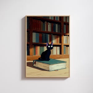 May include: A framed print featuring a black cat with purple ears and large eyes, perched atop a large teal book. The background shows a wooden bookshelf filled with books of various colors. The artwork has a cartoon style.