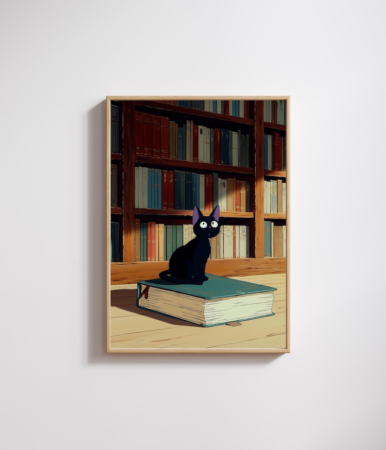 May include: A framed print featuring a black cat with purple ears and large eyes, perched atop a large teal book. The background shows a wooden bookshelf filled with books of various colors. The artwork has a cartoon style.