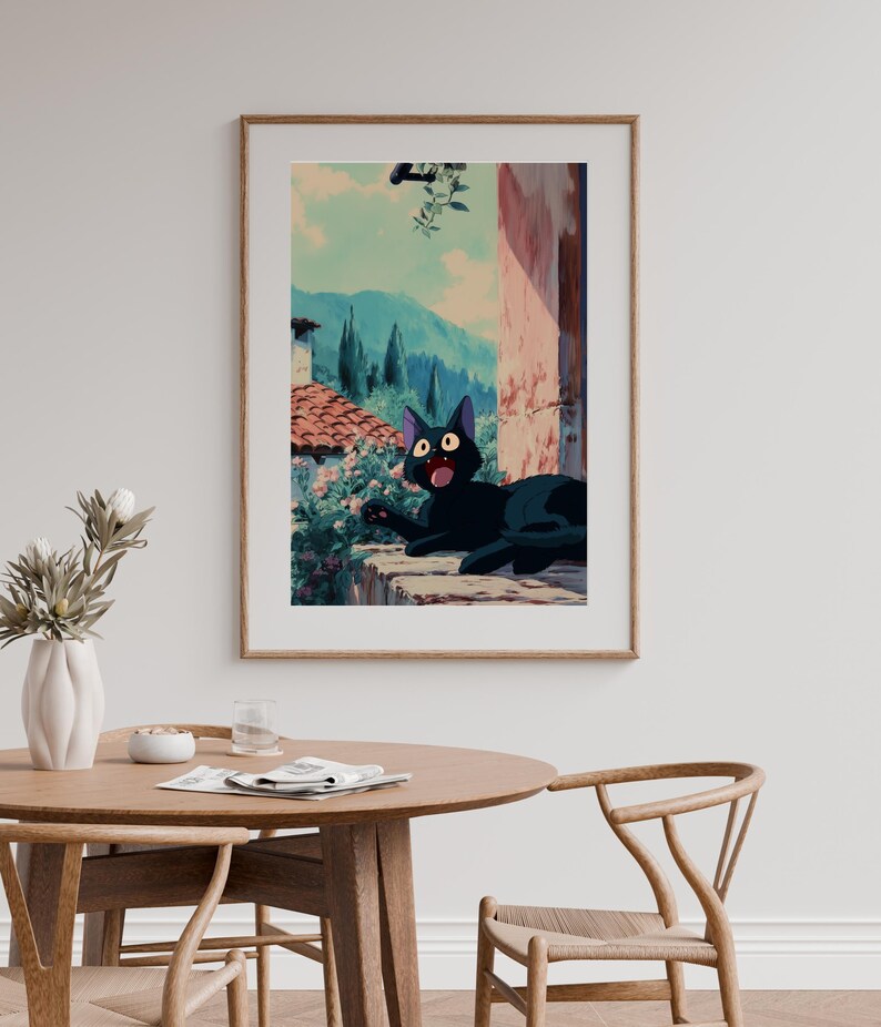 May include: Framed art print featuring a black cat with wide eyes, lounging on a stone ledge. The background depicts a scenic view of mountains, trees, and buildings, with a light blue sky. The artwork has a cartoon style.