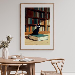May include: A framed print featuring a black cat with large eyes, perched atop a large, teal-colored book. The background shows a library with bookshelves filled with books. The artwork has a cartoonish style.