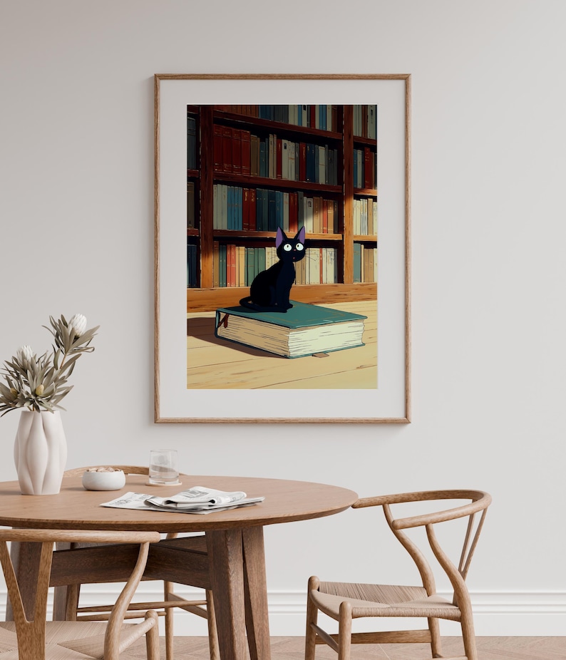 May include: A framed print featuring a black cat with large eyes, perched atop a large, teal-colored book. The background shows a library with bookshelves filled with books. The artwork has a cartoonish style.