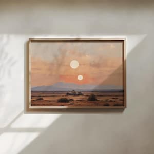 May include: A rectangular framed wall art print featuring a desert landscape under a sunset sky with two circular suns. The scene depicts a flat, arid terrain with low-lying vegetation, distant blue mountains, and small domed structures.