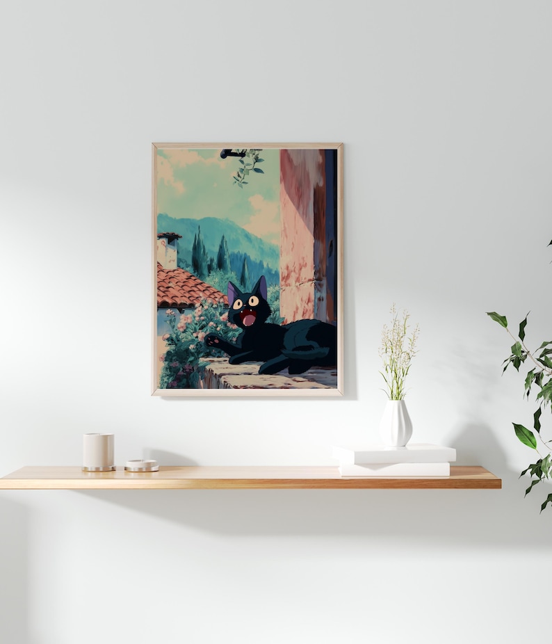 May include: A framed art print featuring a black cat with wide eyes, set against a backdrop of a European village scene. The cat is lying on a stone ledge, with a view of mountains and buildings. The artwork has a vintage, animated style.
