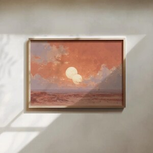 May include: A rectangular framed wall art print featuring a landscape with a desert terrain under a sky filled with orange and peach clouds. Two large, pale circular celestial bodies are visible in the centre of the sky above the horizon line.
