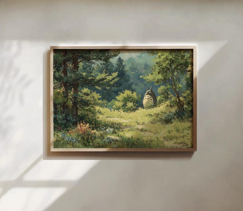 May include: A framed print of a forest scene featuring a large, round, gray creature with pointed ears. The artwork has a light wood frame and depicts a path through a lush green forest with sunlight filtering through the trees.