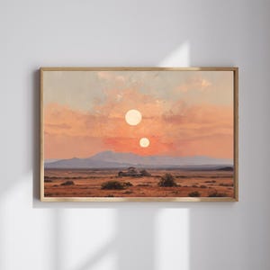 Op de afbeelding: Een ingelijst landschapsschilderij toont een woestijnlandschap onder een zonsonderganghemel. Twee zonnen zijn zichtbaar, met bergen op de achtergrond. Het schilderij zit in een houten lijst.