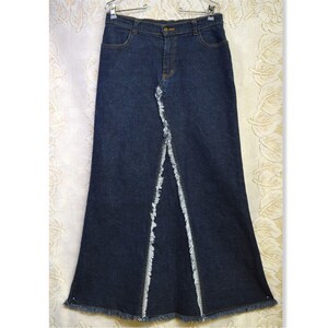 May include: A dark wash denim skirt with a long, flared silhouette. The skirt features a front slit with frayed edges and classic five-pocket styling. The skirt is hanging on a metal hanger.