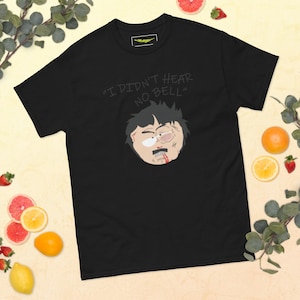 Puede incluir: Camiseta negra con una imagen de dibujos animados de un personaje con un ojo morado y un labio sangriento. El texto "I DIDN'T HEAR NO BELL" está encima de la cabeza del personaje. La camiseta es de material suave.