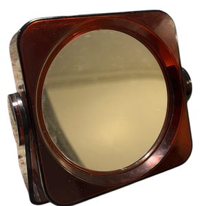 May include: A vintage, square vanity mirror with a circular mirror set within a dark brown frame. The mirror is mounted on a swivel base with a matching brown finish. The frame has a glossy finish.